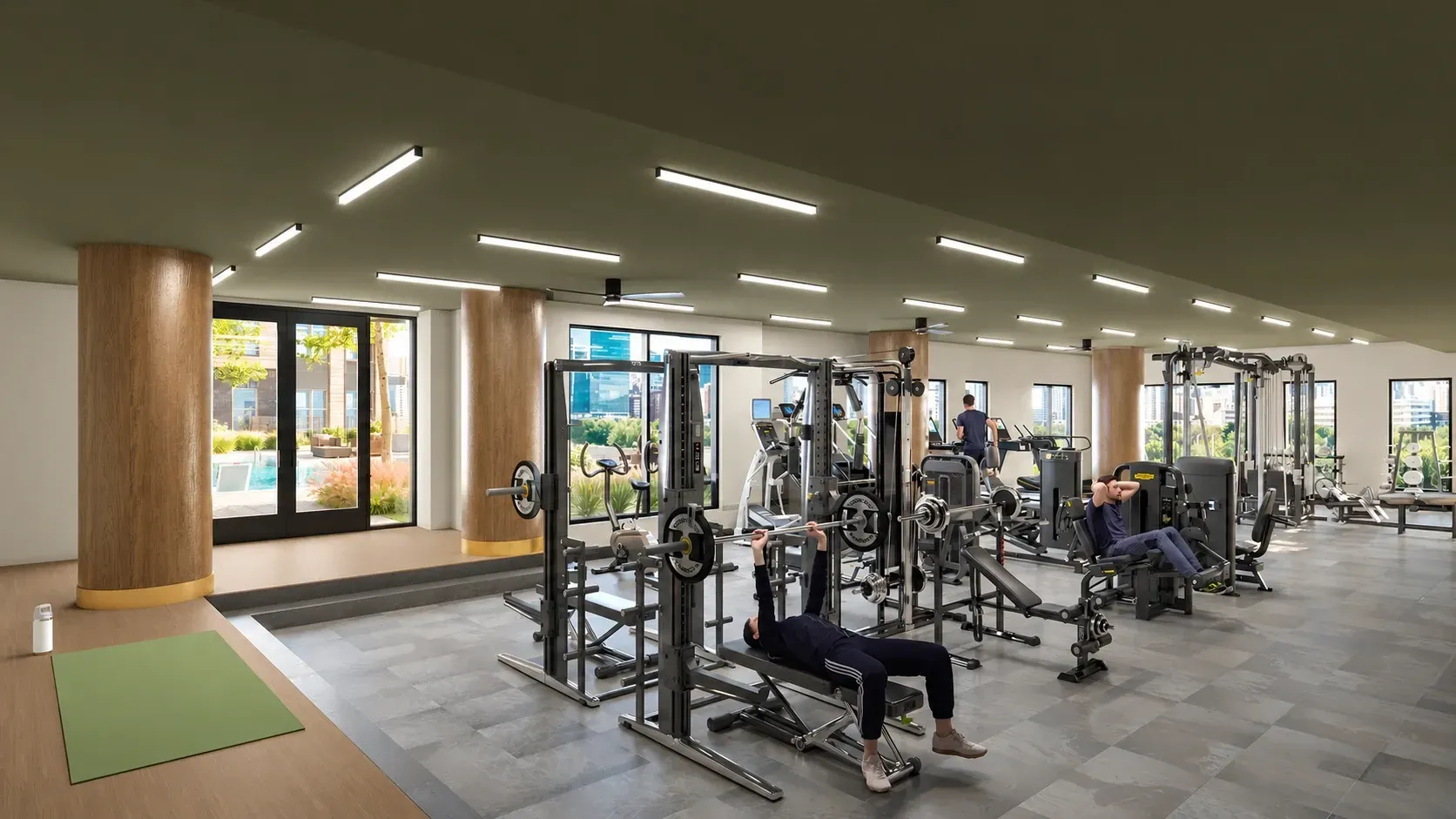 Modern fitness center with cardio and weight training equipment, bright lighting, and large windows overlooking outdoor space.