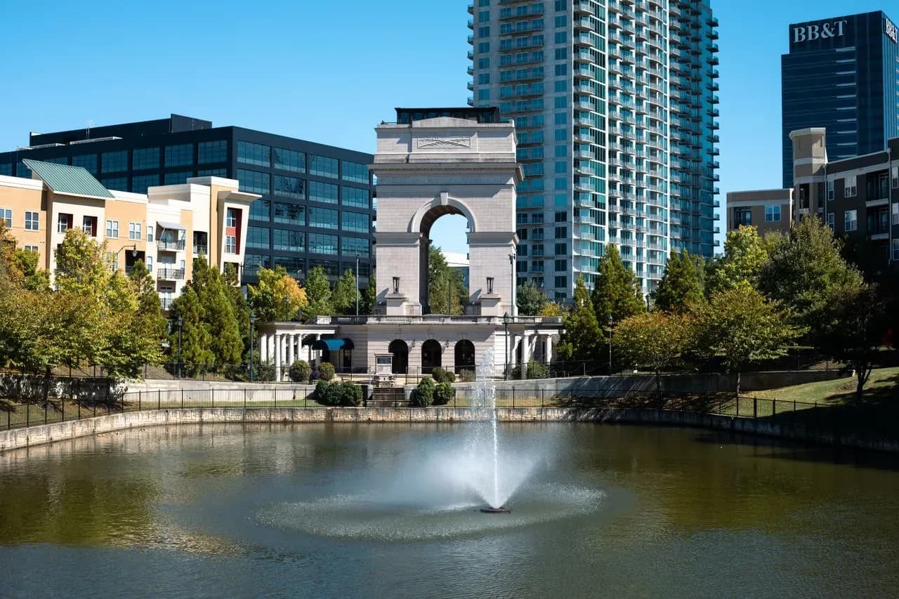 Historic stone monument with fountain in urban riverfront park surrounded by modern buildings